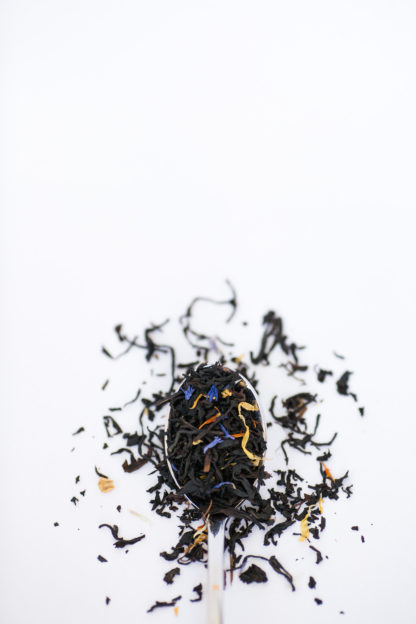 Very dark black tea blended with corn flower petals and yellow marigold petals flow over the silverspoon onto the whtie background