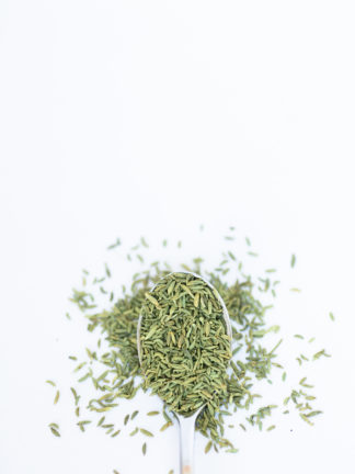 Silver spoon on white background containing green rice-shaped anise seeds