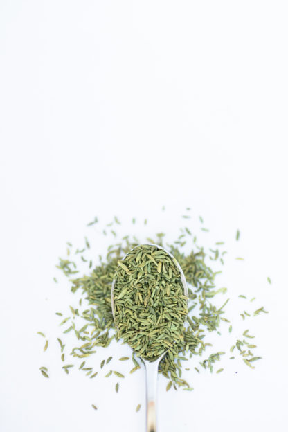 Silver spoon on white background containing green rice-shaped anise seeds