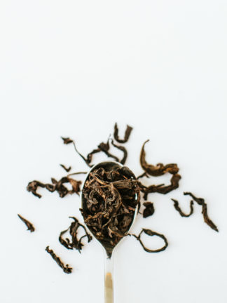 Silver tea spoon overflowing with very long tendril-like tea oolong tea leaves on white background