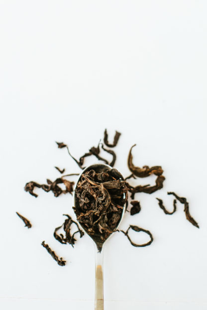 Silver tea spoon overflowing with very long tendril-like tea oolong tea leaves on white background