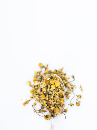 An overflowing spoonfull of chamomile florets on a white background