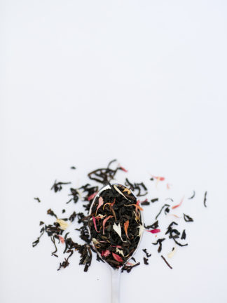 An overflowing silver spoon full of medium length black tea leaves sprinkled with a carnival of naturally colored flower petals on white background
