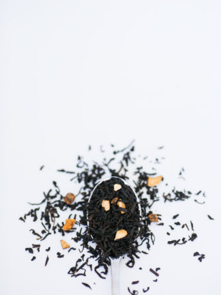 Black tea leaves and dried apricot pieces cascade over the silver spoon onto a white background