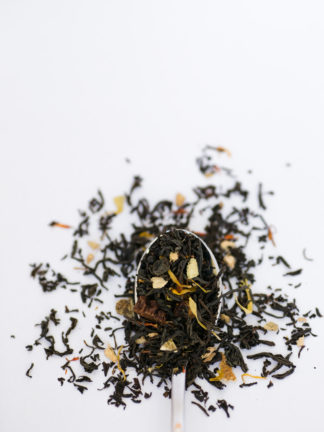 Shredded ginger root blended with orange peel, safflowers and hibisicus petals spill over the spoon onto the white background