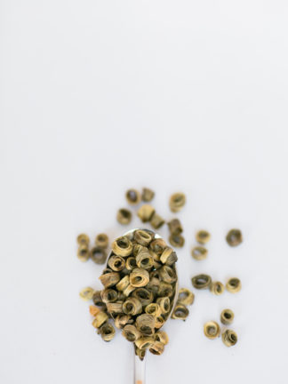Light green and yellow tea leaves wrapped around a hollow center spilling over the silver spoon onto the white background