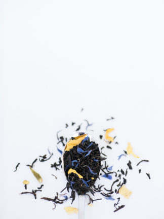 Bright yellow safflowers and dark blue corn flowers blended with dark black tea overflowing a silver spoon onto a white background