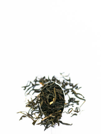 Long and dark green tea leaves are sprinkled with pieces of cream colored jasmine flower petals and flow over the silver spoon onto the pure white background