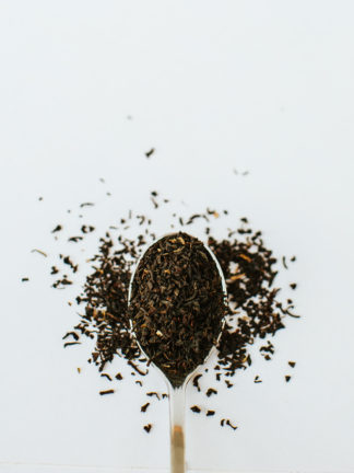 Fine dark tea leaf pieces overflow the silver spoon onto white background