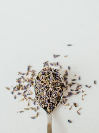 Tiny brilliant purple lavender florets sprinkled from a silver spoon onto to a white background