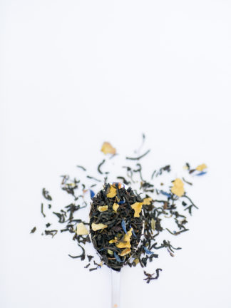 Bright chopped and dried lemon peel mixed with green mint fill the silver spoon and flow onto the white background