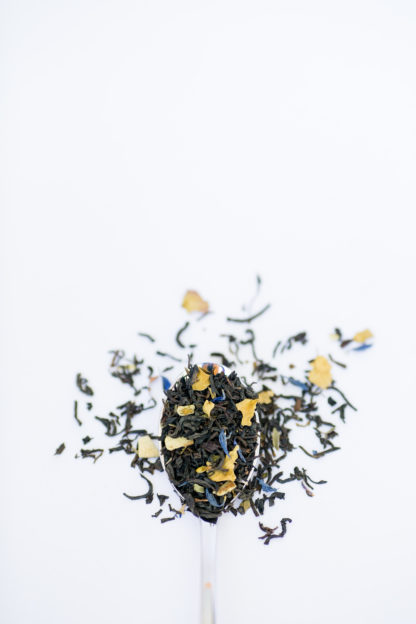Bright chopped and dried lemon peel mixed with green mint fill the silver spoon and flow onto the white background