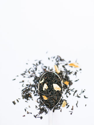 Yellow lemon grass and lemon peal blended with dark brown black tea in silver spoon spilling onto a white background