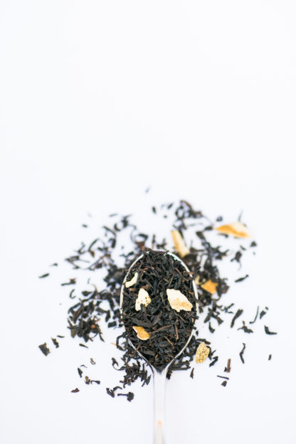 Yellow lemon grass and lemon peal blended with dark brown black tea in silver spoon spilling onto a white background
