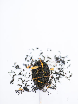 Dried apple and safflower petals blended with dark brown black tea in silver spoon overflowing onto white background