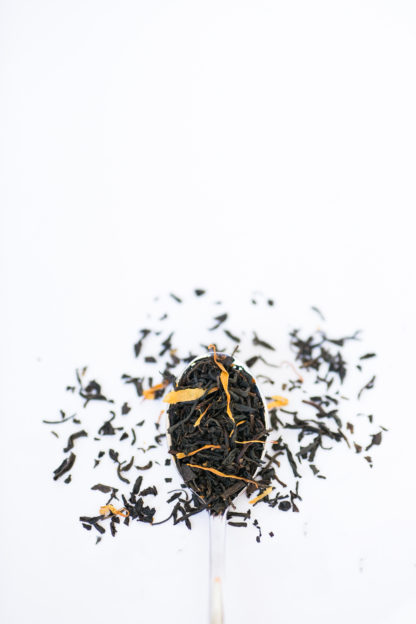 Dried apple and safflower petals blended with dark brown black tea in silver spoon overflowing onto white background