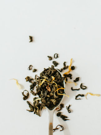 Twisted dark green tea leaves and yellow shredded mango spill over onto a white background