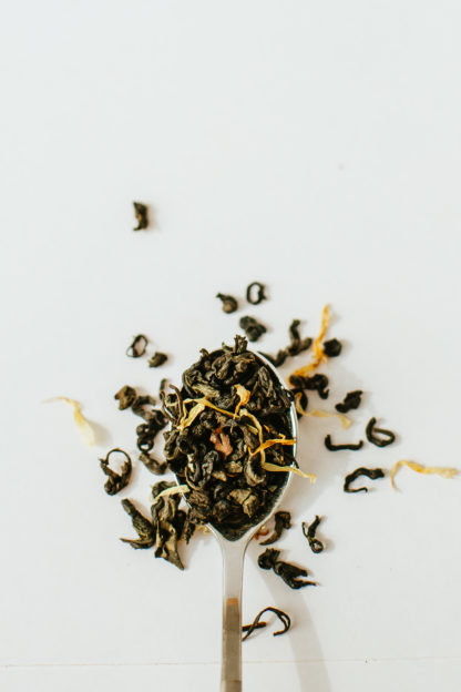 Twisted dark green tea leaves and yellow shredded mango spill over onto a white background