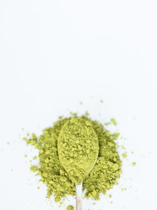 Bright green and very finely ground tea powder spills over the silver spoon onto the pure white background