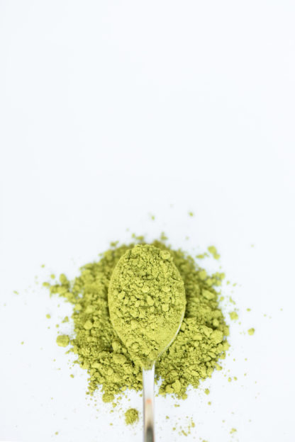 Bright green and very finely ground tea powder spills over the silver spoon onto the pure white background