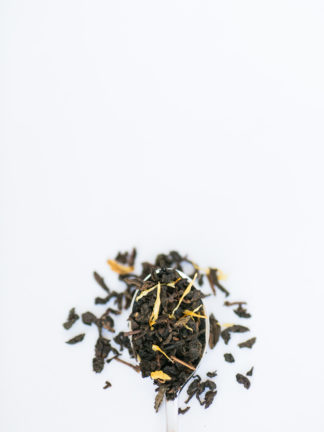 Yellow marigold flower petals are sprinkled among the clumped classic oolong tea leaves overflowing the silver spoon onto the white background