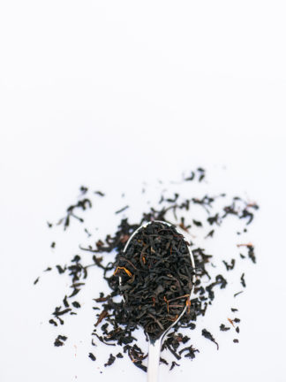 Small black tea leaves sprinkled with orange safflower petals overflow the spoon onto a white background