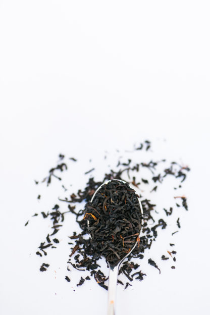 Small black tea leaves sprinkled with orange safflower petals overflow the spoon onto a white background