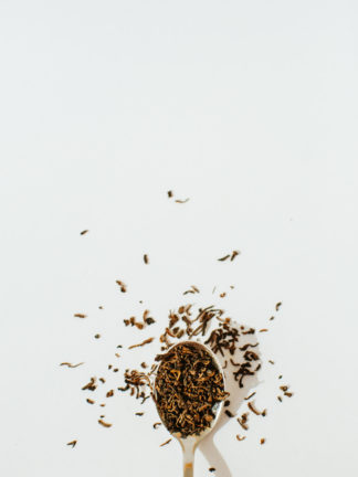 Dark red fermented black tea leaves overflow a silver spoon onto a white background