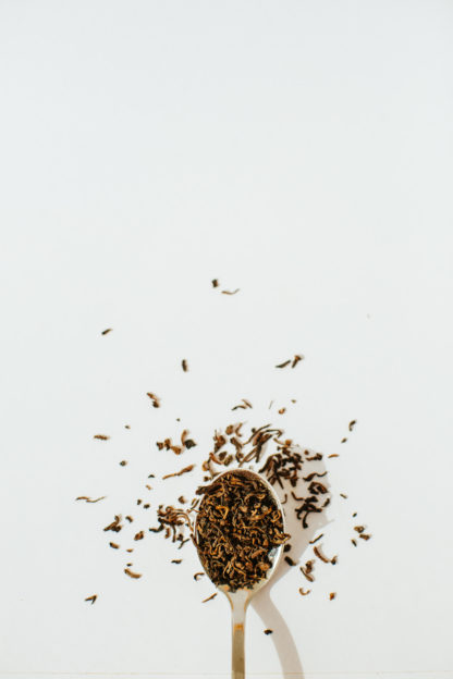 Dark red fermented black tea leaves overflow a silver spoon onto a white background