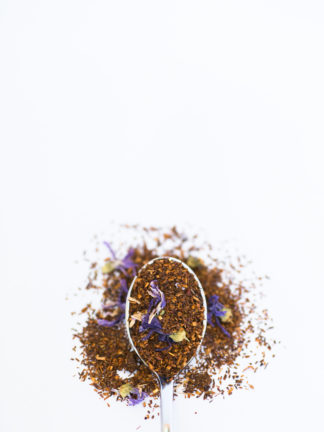 Dark chopped rooibos needles blended with dark purple corn flowers and bright yellow safflower petals fill a silver spoon