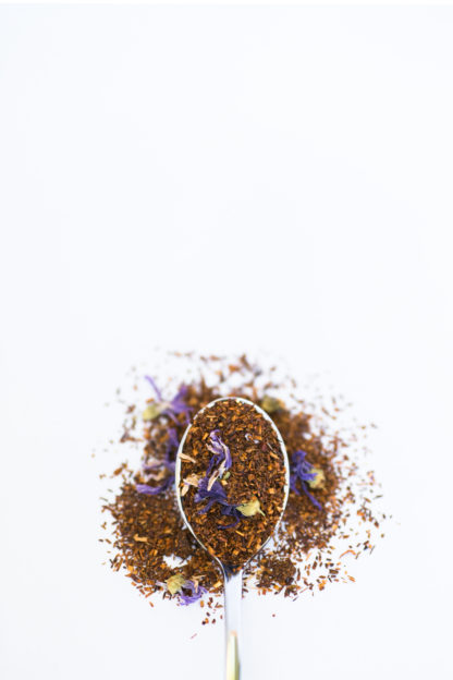 Dark chopped rooibos needles blended with dark purple corn flowers and bright yellow safflower petals fill a silver spoon