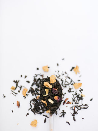 Dark brown black tea leaves blended with lotus flower petals and orange peel cascade over the silver spoon onto the white background