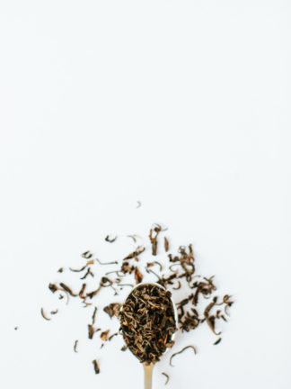 Dark golden brown black tea leaves spill over the spoon onto the white background