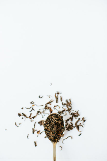 Dark golden brown black tea leaves spill over the spoon onto the white background