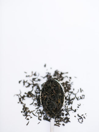 Dark brown black tea leaves overflow the silver spoon onto the white background