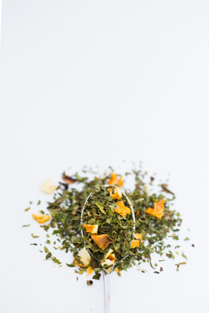 Bright chopped orange skin pieces blended with bright green chopped mint leaves spill over onto a white background