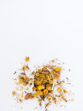 Silver tea spoon cascading dried chamomile flowers on white background