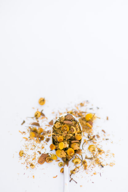 Silver tea spoon cascading dried chamomile flowers on white background