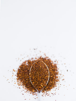 Dark red chopped rooibos with orange flakes spooned onto a white background