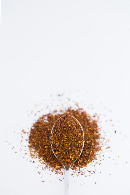 Dark red chopped rooibos with orange flakes spooned onto a white background