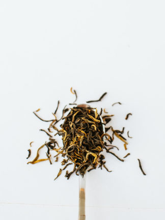Yellow gold tendril tea buds scooped by a silver spoon spilling onto a white background