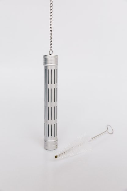 Silver aluminum loose leaf tea tubular infuser with side slits and removeable threaded ends suspended by silver chain with iced tea glass rim hook on a white backgound