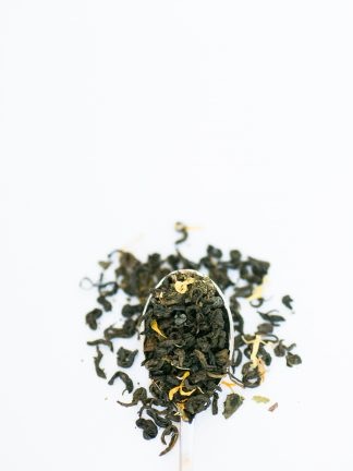 Dark green clumped loose leaf tea leaves mixed with safflowers and mint cascading over a silver spoon on a white background