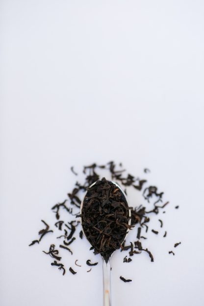 Small dark black tea leaves cascade from a silver spoon onto a white background