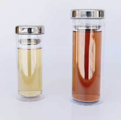 One 12 ounce and one 16 ounce clear glass double walled tea tumbler containing steeped green tea and steeped black tea with a stainless steep strainer separating the liquid and the stainless steel lid on a white background