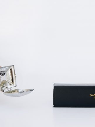 Rectangular silver tea steeping spoon with hinged lid and curved handle in black gift box displayed on a white background